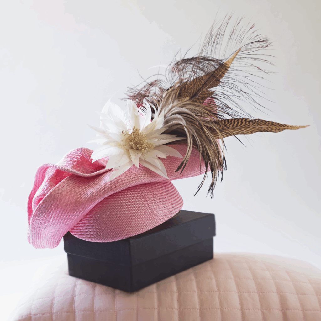 Pink hat with feathers and flowers on top of a black box