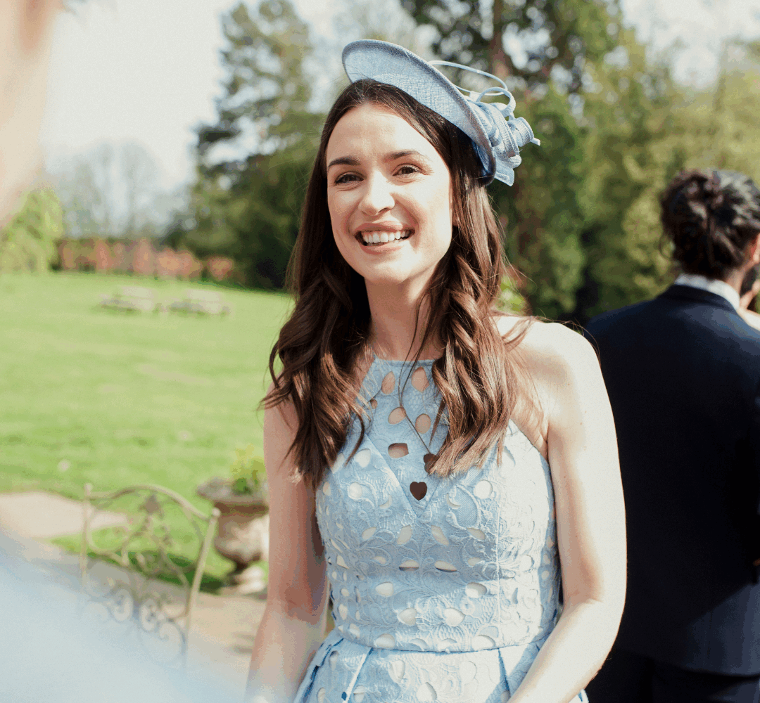 Woman at wedding with long brown hair wearing a pale blue hat that matches her dress.